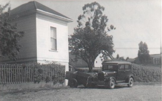 A scan of a quite old black and white photo of an old, modest house in northern California, with an old 1928 Model A Ford parked in front of it, and a large cherry tree in the front yard