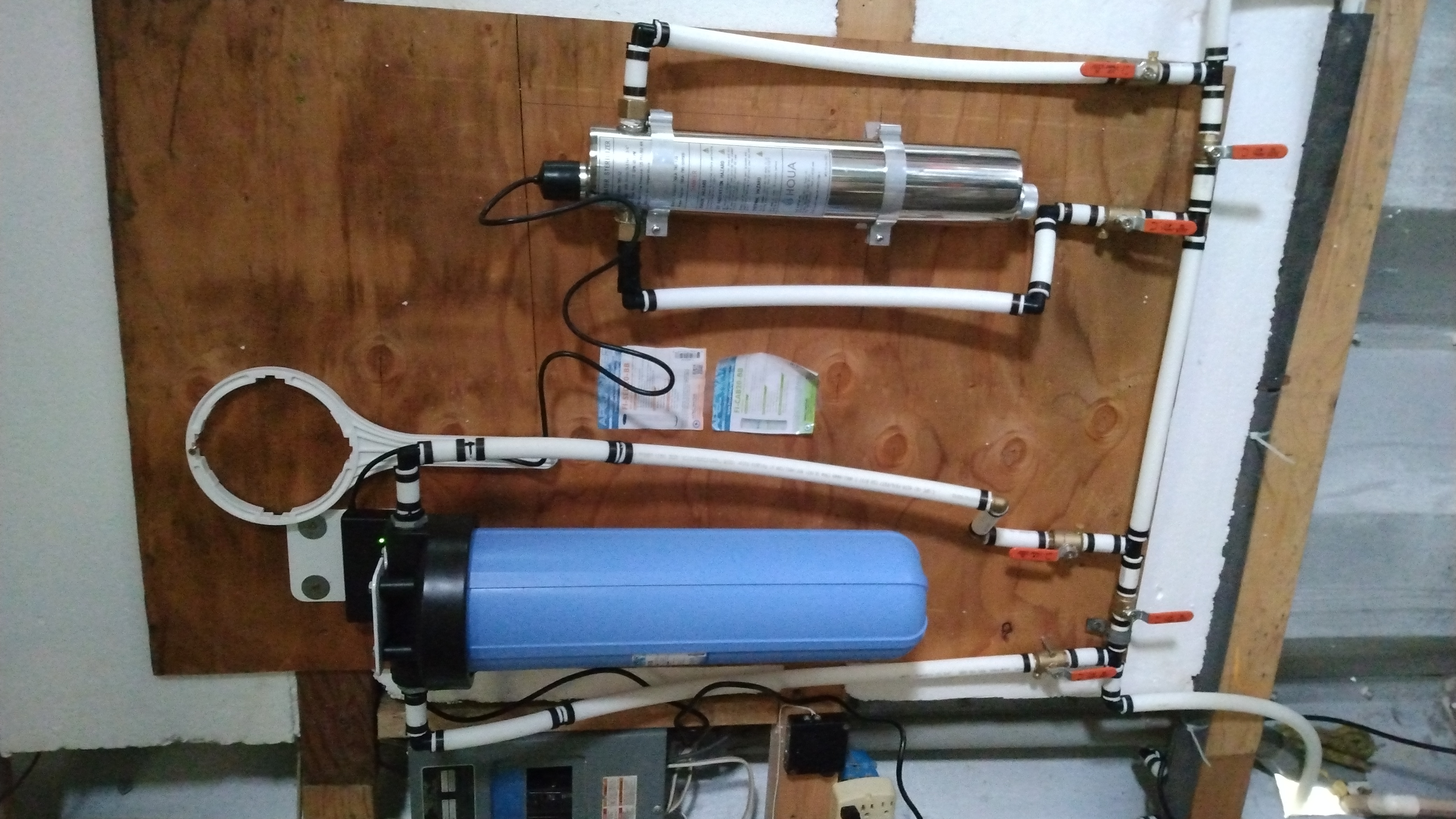 Some pipes attached to a piece of plywood, in an arrangement with valves such that two filters (a paper large filter and UV-light filter) can be activated or isolated